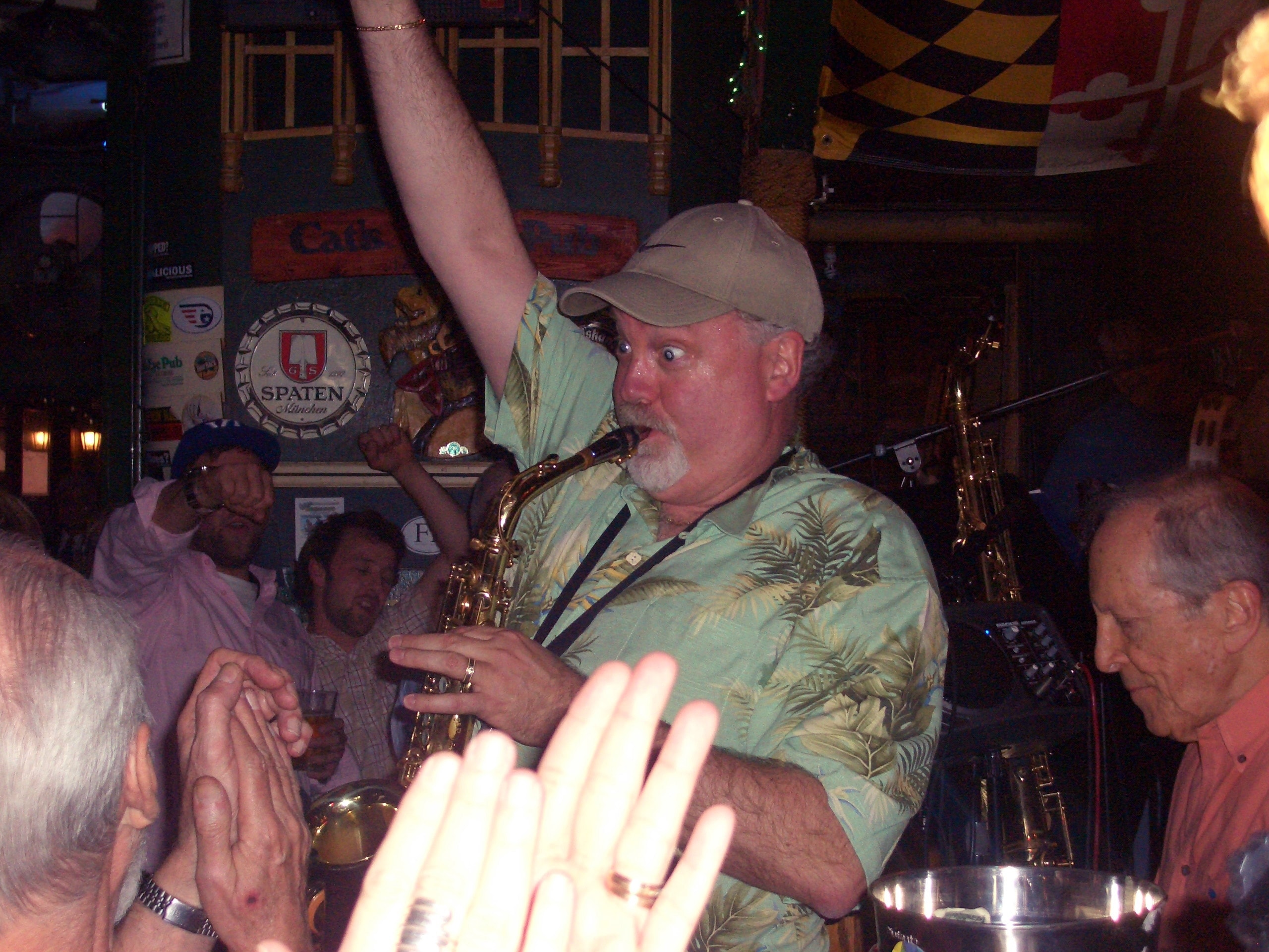 Jay playing saxophone in a packed bar, crowd hands raised
