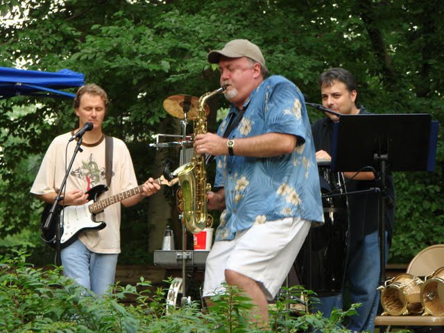 Band performing outdoors at Lurman — guitar, saxophone, and flute